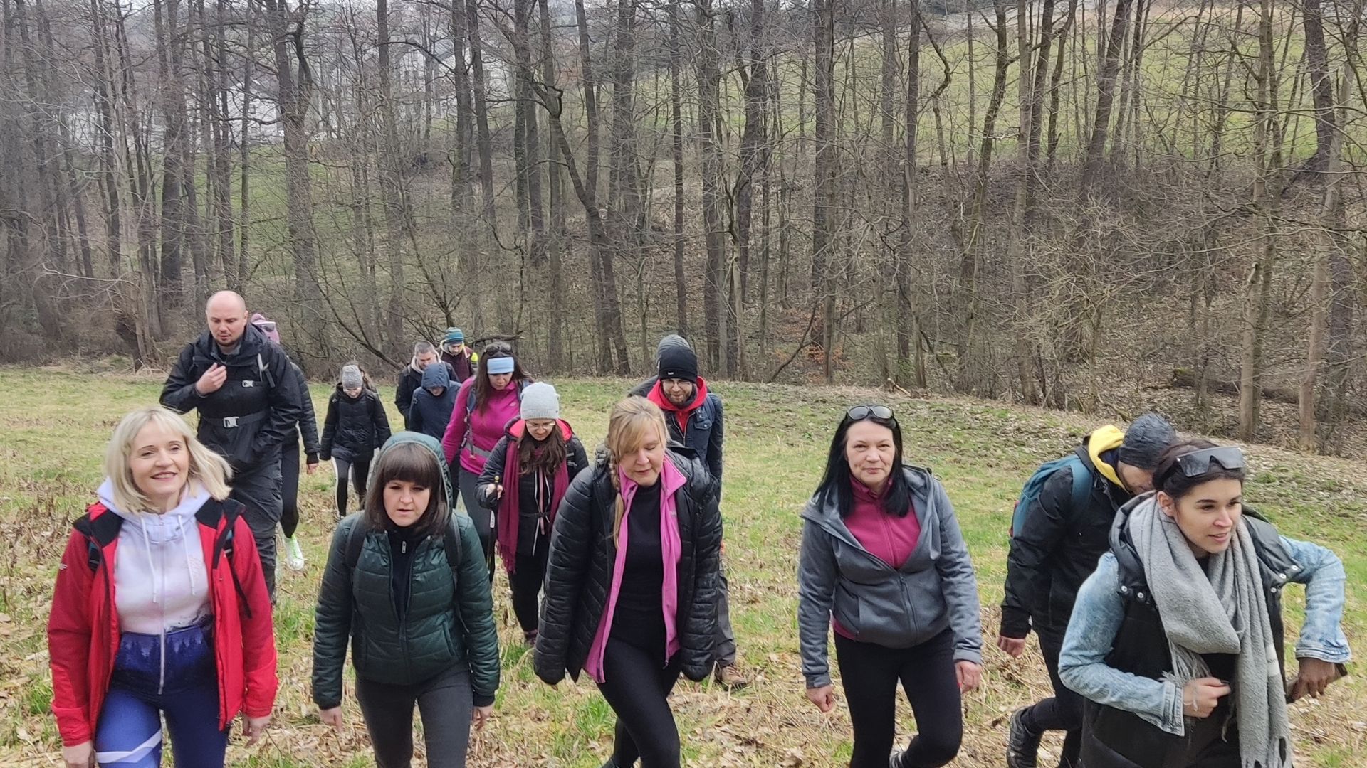 Grupa osób idzie wspólnie pod górę leśną ścieżką podczas wędrówki integracyjnej, ubrani w sportowe i trekkingowe stroje.