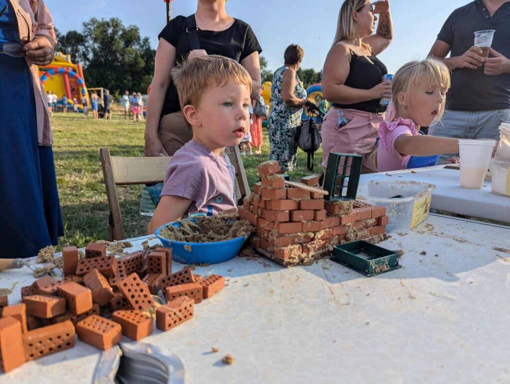 Dzieci uczestniczą w warsztatach budowlanych Majster Klub podczas wydarzenia plenerowego