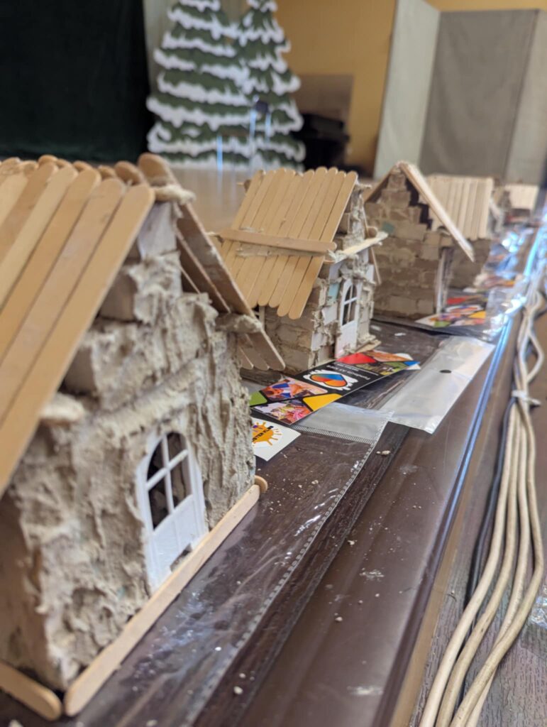 Rząd miniaturowych domków wykonanych z zaprawy, małych cegiełek i drewnianych patyczków po lodach ustawionych na stole.